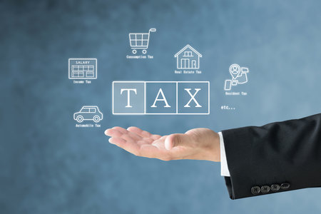 A man's hand in a suit holding up various tax icons and the word TAXの写真素材