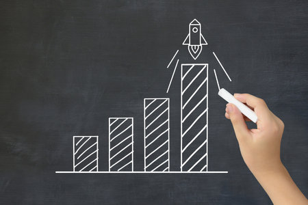 A child's hand drawing an upward-sloping bar graph with a rocket - an image of improving grades and academic abilityの写真素材