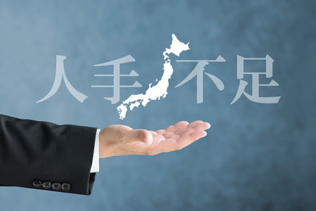 The hand of a person in a suit holding up a map of the Japanese archipelago and the words "Labor Shortage"の写真素材
