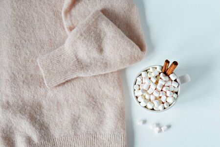 Light pink wool sweater, pine cons and cup with marshmallows and cinnamon on the wooden deskの写真素材