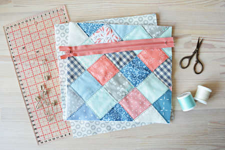 Working process: quilt, zipper, threads, retro scissors , quilting pins and ruler on the wooden...