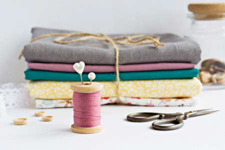 Vintage pink thread spool , pins, wooden buttons in jar, retro scissors and cotton fabrics