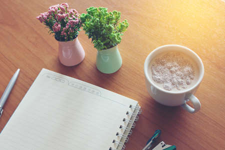 A hot cup of coffee to handle a notebook, a pen, a calculator, Staples and a vase on the table.の写真素材