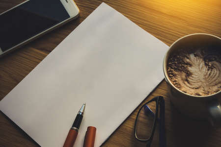 blank notepad with spectacles, coffee, pen and smart phone on a wooden table, retro style.の写真素材