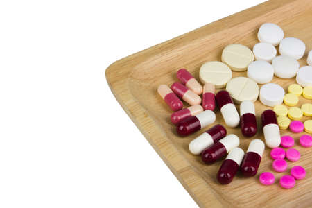 Assorted pharmaceutical medicine pills, tablets and capsules on wooden tray