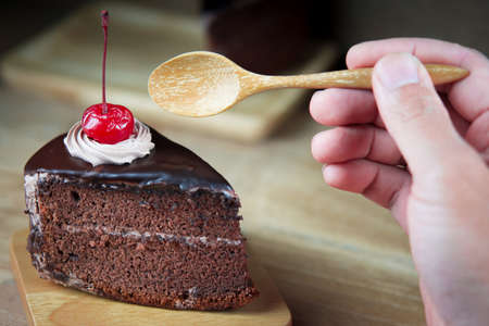 Closeup of a hand holding a knife about to slice into a chocolate cake on wooden tables,