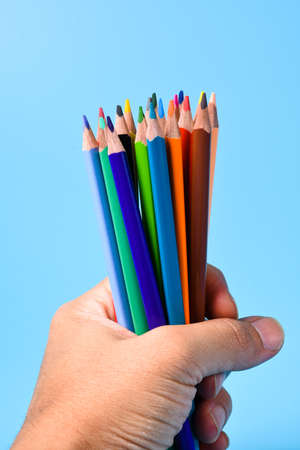 Hands holding a bunch of pencils on a blue backgroundの写真素材