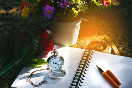 Pocket watch and pen on a blank white notebook on table