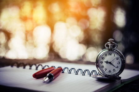Pocket watch and pen on a blank white notebook on tableの写真素材