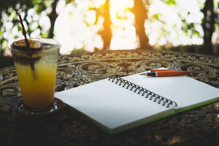 Fresh passion fruit juice in glass on table with is tree garden background, notepad and pen
