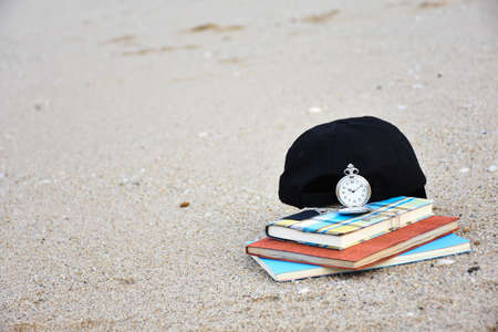 A cap is placed near the clock. And the book stack is placed on the beach.の写真素材