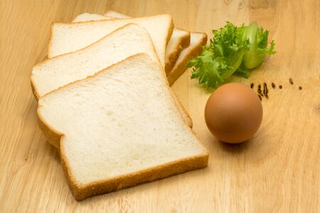 Pile of sliced bread, egg and vegetable on wooden board