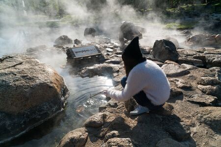 Teen girl boiling eggs in hot water in front of a board showing the highest temperature of water at hot spring in Jae Sawn National Park, Lampang, Thailandの写真素材