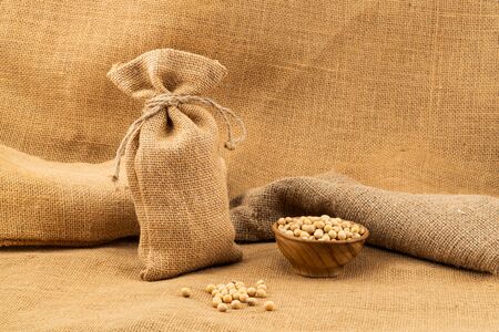 Soy beans in a sack and in a wooden bowl on sackcloth.の写真素材