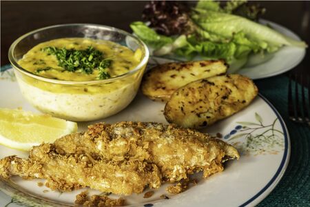 Fried fish with vegetables and piece of lemon on ceramic plate.の写真素材