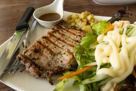 Pork steak with black pepper, potato and vegetable in white plate on wooden table.の写真素材