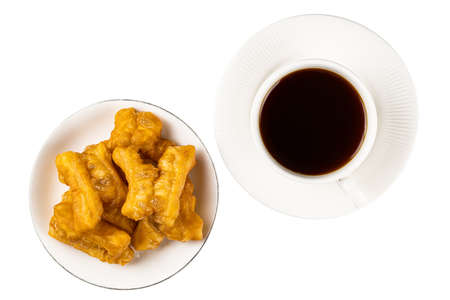 Top view of deep-fried dough stick in a whte plate and black coffee in white ceramic cup on white...