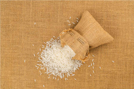 Top view of jasmine rice flow out from a sack on the floor covered with sackcloth.の写真素材