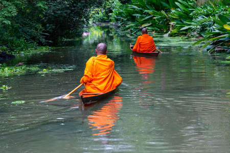 Buddhist monks paddle boat in the canal. Two monks row the small wooden boat in a canal to receive alms from Thai people in the morning.の写真素材
