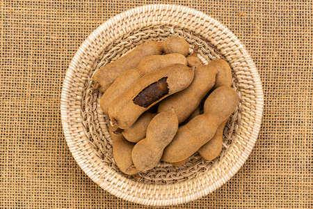 Top view of tamarind in a bamboo basket on sackcloth. Ripe whole and peeled tamarind in bammboo basket.の写真素材