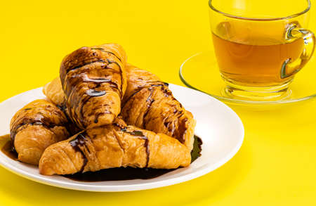 View pile of homemade croissants poured with chocolate topping in white ceramic dish and a cup of...