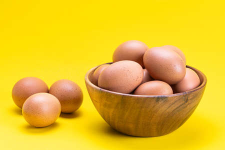 Side view of fresh chicken eggs in wooden bowl and on yellow backgroundの写真素材