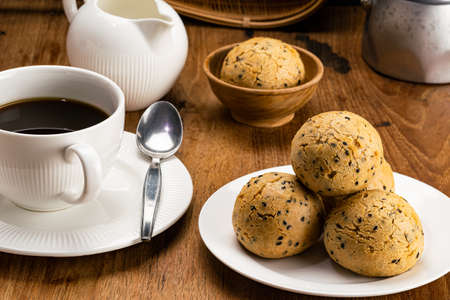 Closeup view pile of sesame mochi bun in white ceramic plate, a cup of black coffee with metal...