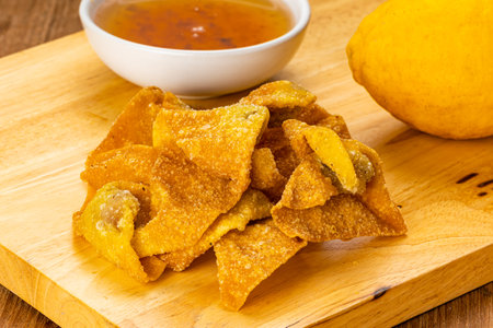 High angle view pile of delicious crispy homemade deep fried wontons on wooden cutting board with sweet dipping sauce in white ceramic cup and ripe lemon on wooden table.の写真素材