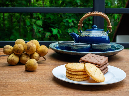 Teatime with hot chinese tea in beautiful design blue set, round and square shape crackers in white ceramic dish and ripe sweet tropical fruit 'long kong'.の写真素材