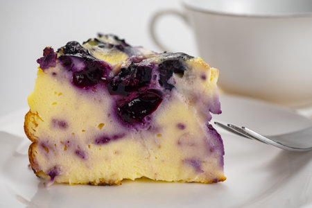 Closeup view slice of yogurt blueberry cake with metal fork in white ceramic dish and a cup of coffee.の写真素材