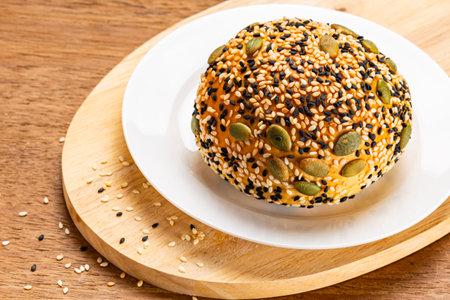 High angle view of burger bun sprinkled with white and black sesame and pumpkin seeds in white...
