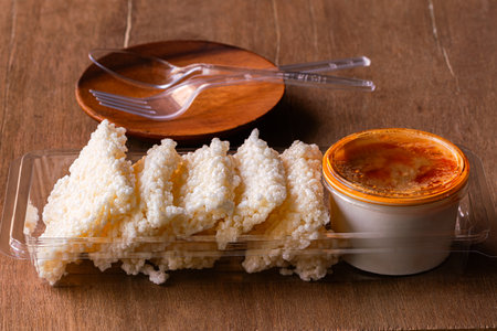 Crispy rice cracker with savory dipping sauce in simple plastic container with fork and spoon on wooden table.の写真素材