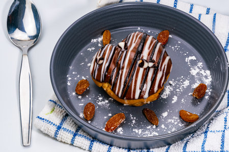 Chocolate choux cream pastry with raisins in black ceramic dish on kitchent cloth and metal spoon on...