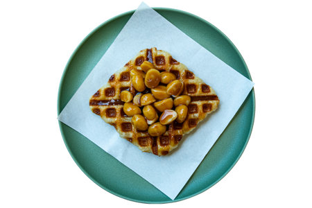 Top view of caramel macadamia nuts waffle or croffle on white paper in green ceramic plate isolated on white background with clipping path.の写真素材