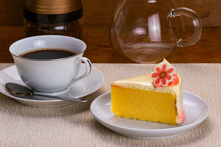 Side view of a slice of vanilla sponge cake garnished with cream in white ceramic dish and a cup of...