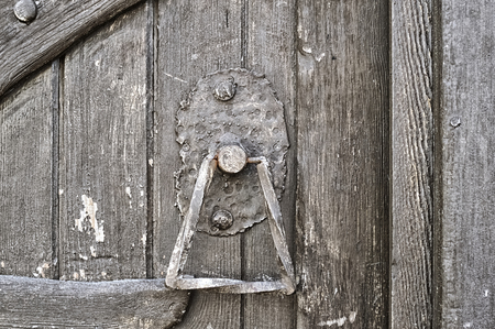 Wrought iron door handle on rough wooden old door made of painted boardsの写真素材