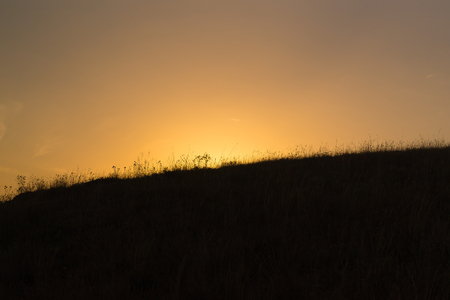 Beautiful sunset backlight behind the hill with grassの写真素材