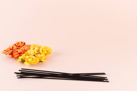 Black incense sticks with orange and yellow flowers on pink background with place for textの写真素材