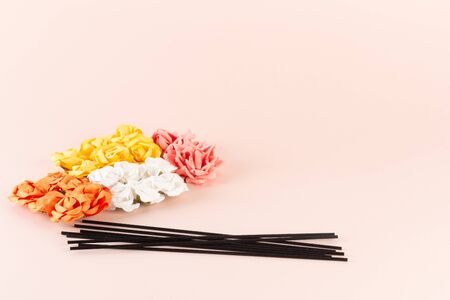 Black incense sticks with white, pink and yellow flowers on pink background with place for textの写真素材
