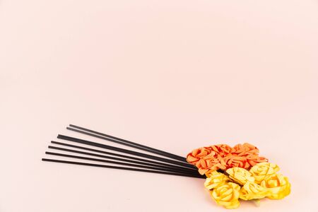 Incense sticks with orange and yellow flowers on pink background with place for textの写真素材