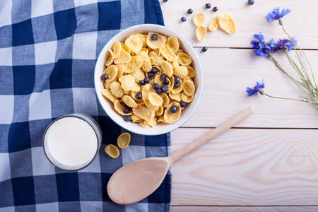 cornflakes with bilberry, milk cup , flower and spoon on wooden tableの写真素材