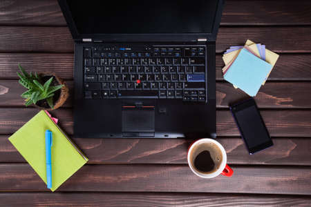 Workplace with  computer, phone, notepad, cup of black coffee on wooden tableの写真素材