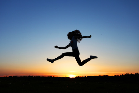 silhouette of female jumper in sunset sky having funの写真素材