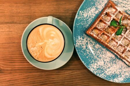 Waffles  with sugar powder and cup of coffee on wooden table. Top view.