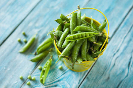 Fresh green peas in yellow bucket on vintage wooden tableの写真素材