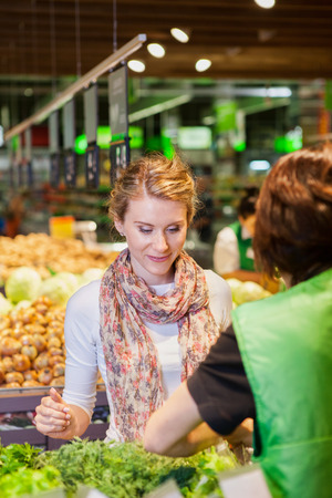 Portrait of beautiful young woman choosing green leafy vegetables in grocery store. Concept of healthy food shoppingの写真素材
