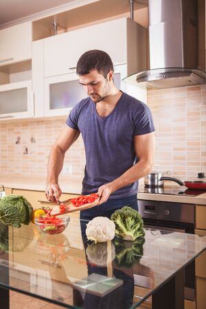 Casual man preparing salad at home in kitchen.の写真素材