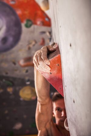 Muscular man practicing rock-climbing on a rock wall indoors closeupの写真素材