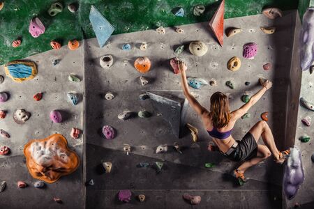 Young woman climbing up on practice wall in gymの写真素材
