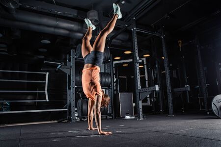 Attractive young athlete with muscular body exercising crossfit. Walking on her hands standing...
